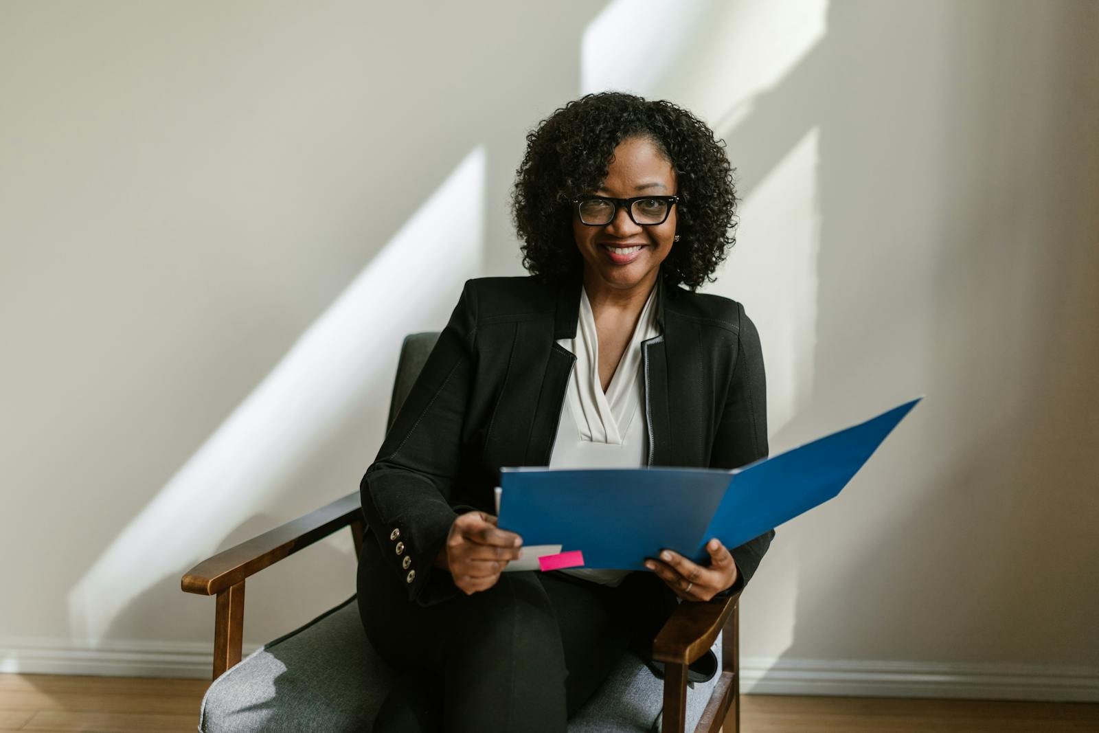 Home Professional African American woman with glasses and curly hair holding a blue folder indoors.